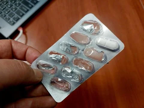 Hand Holding Blister Pack With Tablets on Wooden Surface During Work Hours Stock Photos