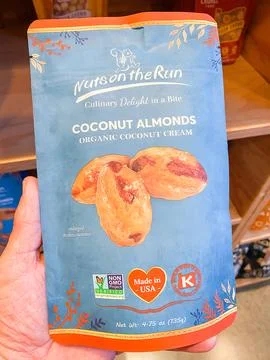 A hand holding a blue package of Nuts on the Run Coconut Almonds - August 0.. Fotos de archivo