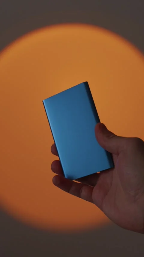 Hand holding a blue portable external SSD drive on orange sunset lamp backg.. Stock Footage 335143219