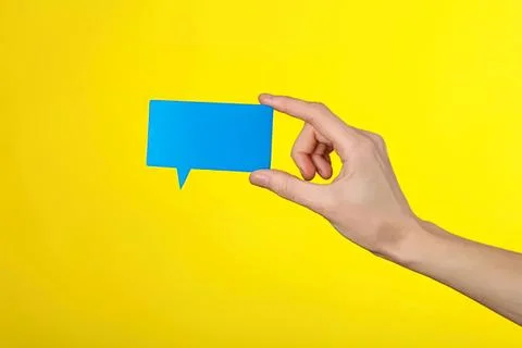 Hand holding blue speech bubble on yellow background Stock Photos