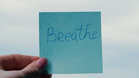 Hand holding blue sticky note with handwritten word Breathe against sky Stock Photos