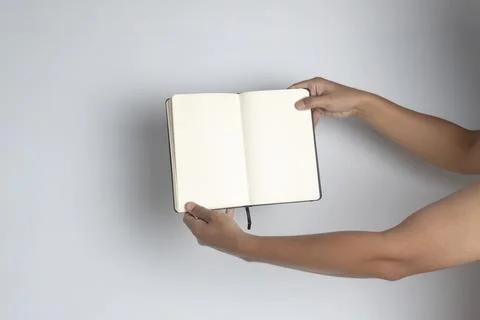 Hand holding a book with a plain black cover isolated on a white background.. Stock Photos