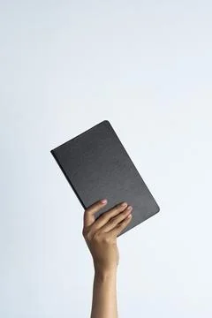 Hand holding a book with a plain black cover isolated on a white background.. Stock Photos