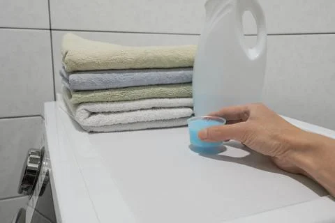 Hand holding a bottle of laundry detergent and towels on a washing machine Stock Photos