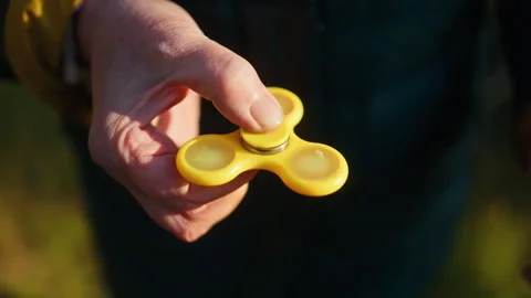 A hand holding a bright yellow fidget spinner in a beautiful natural setting a Stock Footage 308335587