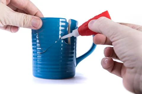 Hand holding a broken piece while applying glue to a hole in a cup Stock Photos