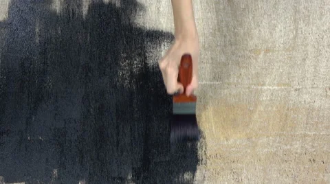 Hand holding a brush applying black paint on a wooden surface. Video stock 66529373