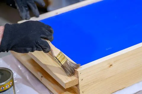 Hand holding a brush applying varnish paint on a wooden garden table - pain.. Stock Photos