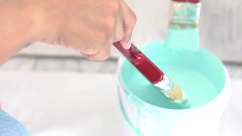 Hand holding brush dipprd in a bucket of paint Stock Footage 250388937