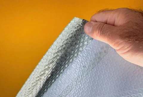 Hand holding bubble wrap packaging material against yellow backg 库存照片