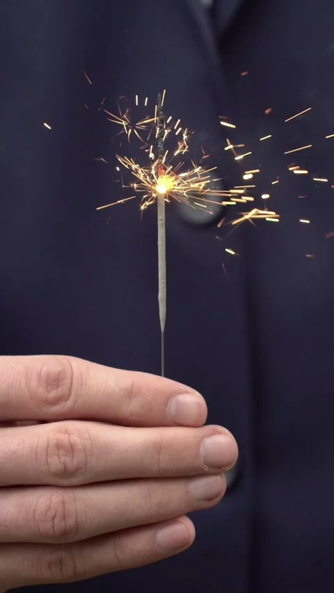 Hand holding a burning sparkler against a dark navy business suit Stock Footage 344891241