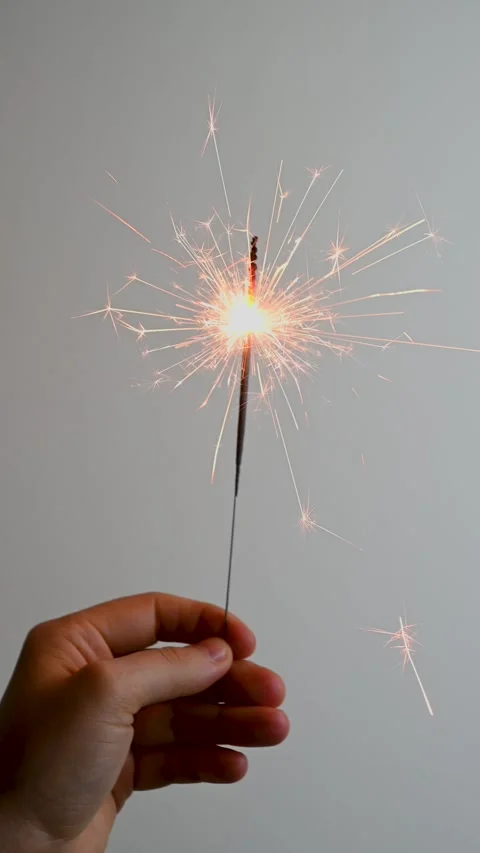 Hand holding burning sparkler sparkling against neutral indoor wall Stock Footage 331585893