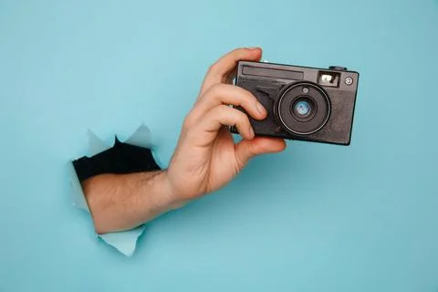 Hand holding camera from blue torn paper Stock Photos