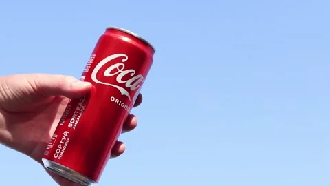 Hand holding a can of Coca-Cola against a blue sky background Stock Footage 334240613