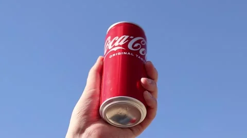 Hand holding a can of Coca-Cola against a blue sky background Stock Footage 334240679