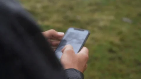 Hand holding a cellphone and tapping on screen in nature, slow motion Stock Footage 129610949