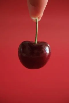 Hand holding a cherry on red background Stock Photos