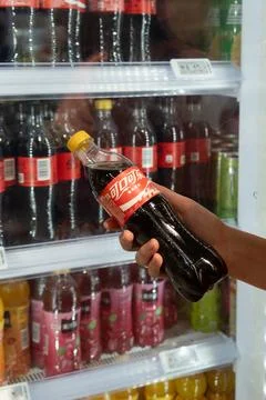 Hand holding China version Coca-Cola bottle in front of supermarket fridge Stock Photos