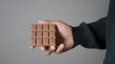 Hand holding a chocolate bar in a simple setting 스톡 동영상 330566116