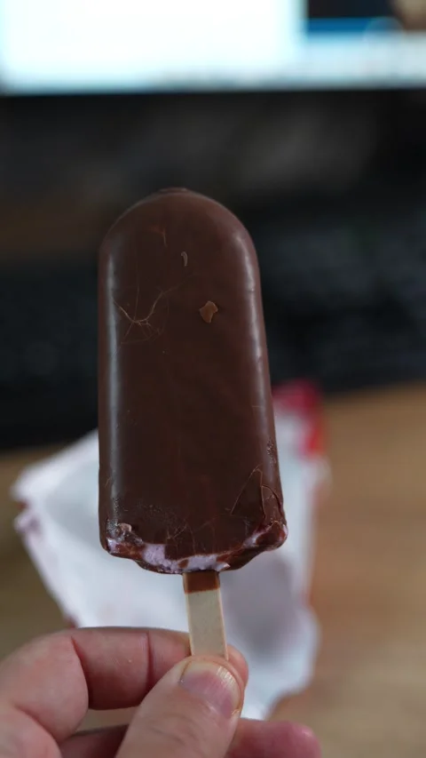A hand holding a chocolate covered ice cream bar on stick Stock Footage 332781003