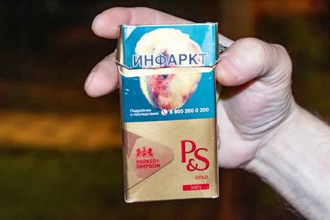 Hand holding cigarette pack with warning label about heart attack risk Foto stock