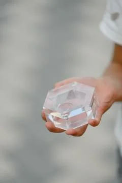 Hand holding clear hexagonal crystal object with reflections and shadows Stock Photos
