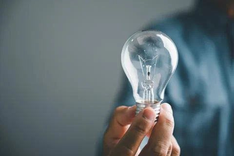 Hand holding a clear lightbulb, symbolizing new ideas and inspiration.  Sim.. Stock Photos