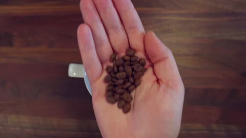 Hand holding coffee beans over morning coffee with cream Vídeos de archivo 130403899