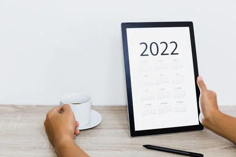 Hand holding coffee cup while looking calendar on digital tablet. 스톡 사진