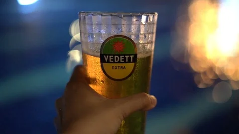 Hand holding cold vedett draft beer glass with blue pool bokeh flicker Stock Footage 106495254
