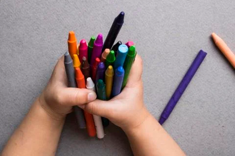 A hand holding colored crayons on gray paper. Flat lay Stock Photos