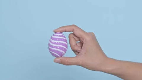 Hand holding colorful Easter egg on blue background. Easter holiday decoratio Stock Footage 149813404