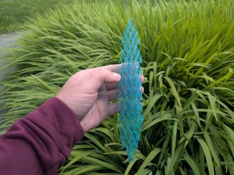 A hand holding a complex, 3D-printed blue geometric lattice strip toy Stock Photos