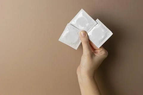 Hand holding condom packets on color background, contraception and safe sex Stock Photos