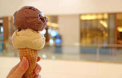 Hand holding cone with two scoops of chocolate and peanut butter ice cream Stockfoto's