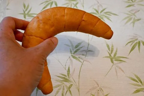 Hand holding a crescent-shaped bread roll Foto stock