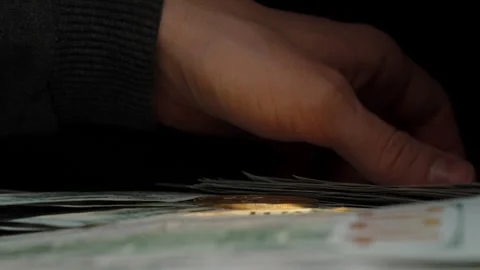 Hand Holding a Crisp US 100 Dollar Bill with a Stack of Cash Below. Symbolizing Stock Footage 296565476
