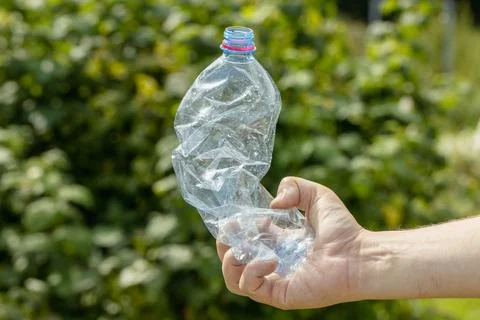 Hand holding crumpled empty plastic bottle in the park Stock Photos
