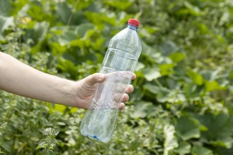 Hand holding crumpled empty plastic bottle in the park Stock Photos