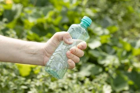 Hand holding crumpled empty plastic bottle in the park Stock Photos