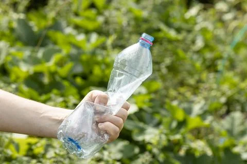 Hand holding crumpled empty plastic bottle in the park Stock Photos