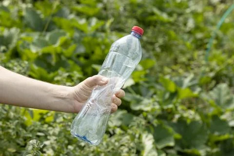 Hand holding crumpled empty plastic bottle in the park Stock Photos