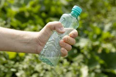 Hand holding crumpled empty plastic bottle in the park Stock Photos