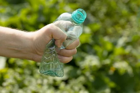Hand holding crumpled empty plastic bottle in the park Stock Photos