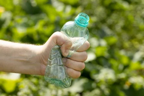 Hand holding crumpled empty plastic bottle in the park Stock Photos