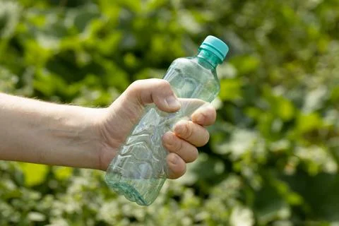 Hand holding crumpled empty plastic bottle in the park Stock Photos