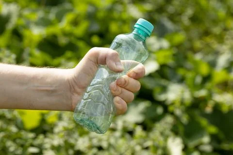 Hand holding crumpled empty plastic bottle in the park Foto stock