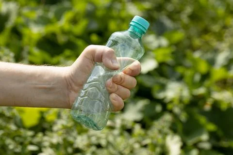 Hand holding crumpled empty plastic bottle in the park Stock Photos