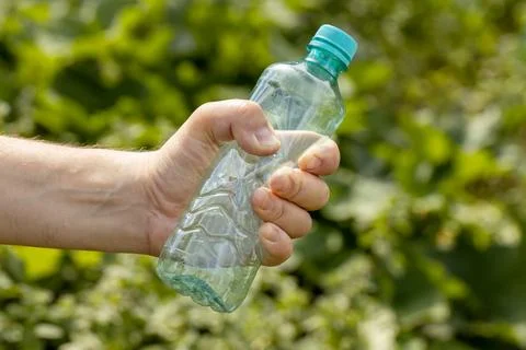 Hand holding crumpled empty plastic bottle in the park Stock Photos