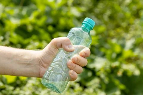 Hand holding crumpled empty plastic bottle in the park Stock Photos